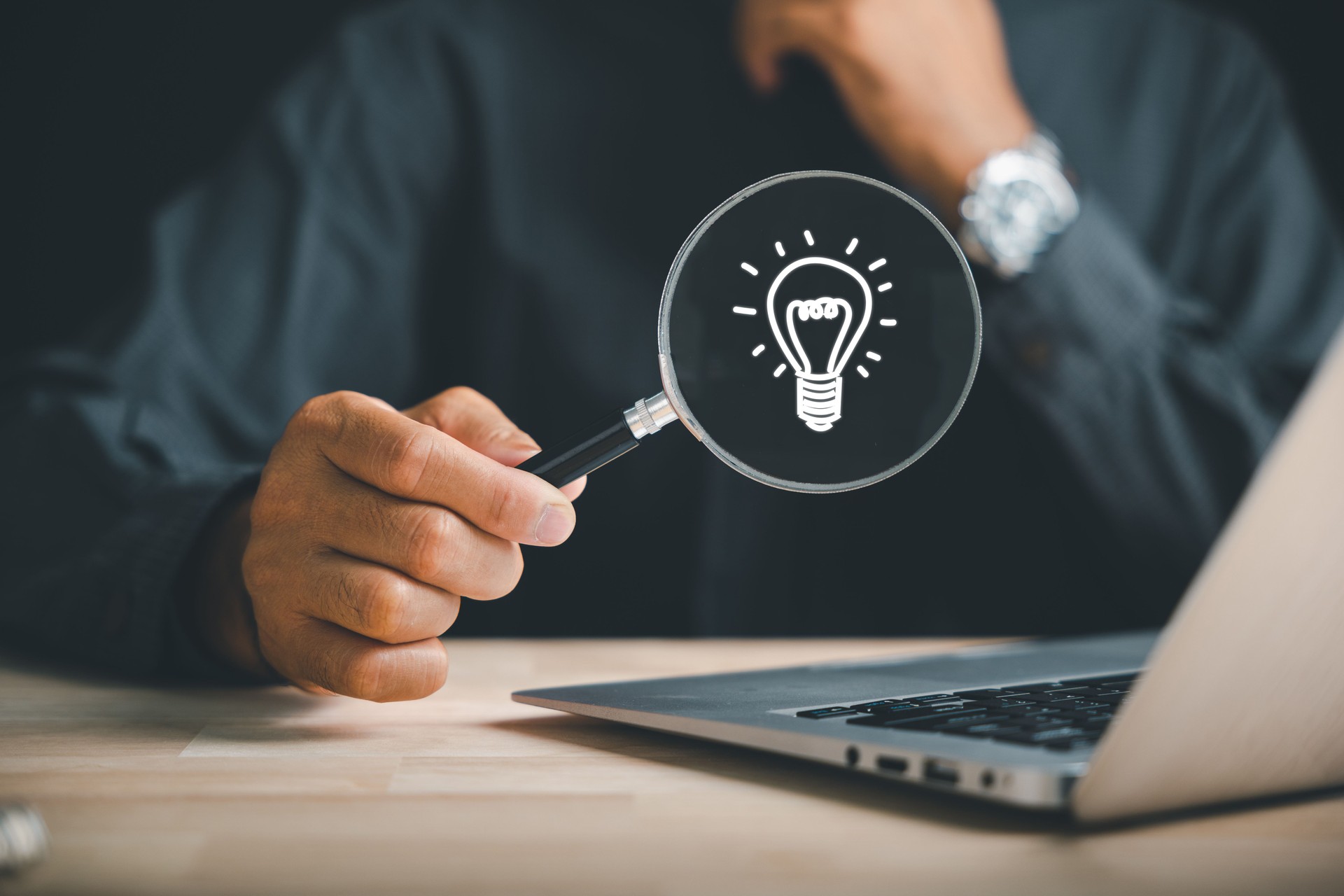 Magnifying glass in businessman's hand reveals light bulb